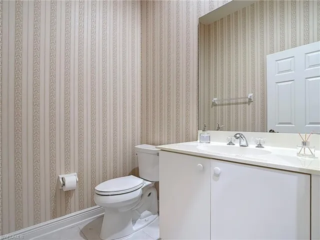 Half bathroom with toilet, wallpapered walls, and vanity