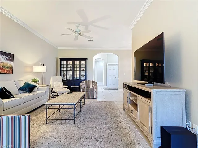Living area with  arched walkways, light tile patterned flooring, and crown molding