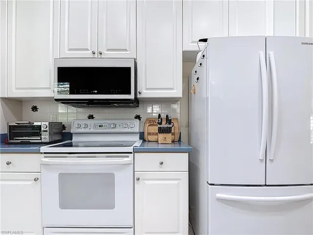 Kitchen featuring white appliances, backsplash, and white cabinets.
