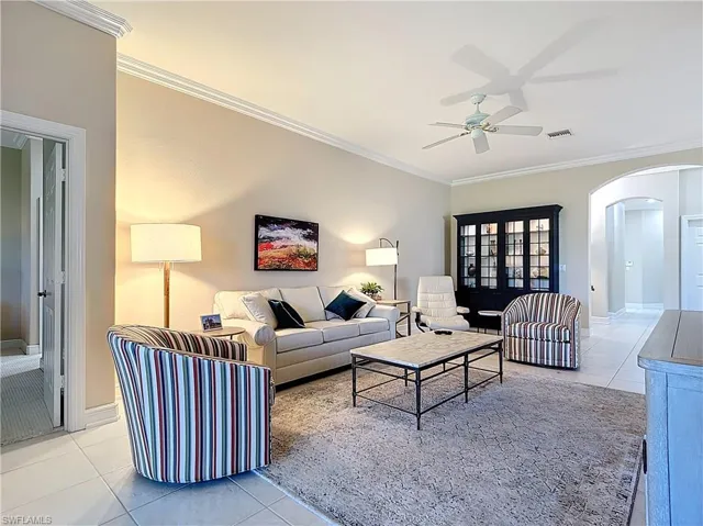 Tiled living room with ceiling fan, arched walkways, crown molding.