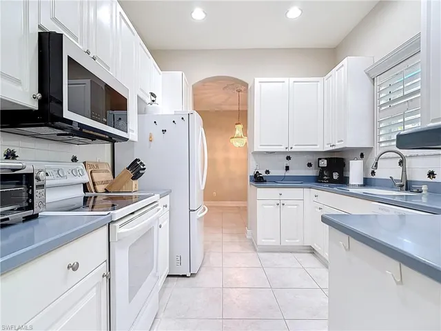 Kitchen featuring white appliances, backsplash, and white cabinets