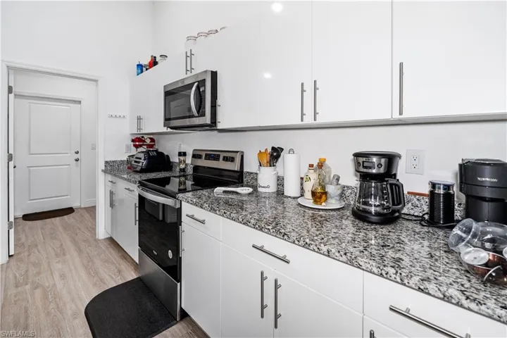 Kitchen featuring stainless steel appliances, white cabinets, dark stone counters, and light wood-style flooring