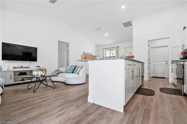 Kitchen featuring white cabinets, dark stone counters, vaulted ceiling, a peninsula, and light wood-type flooring