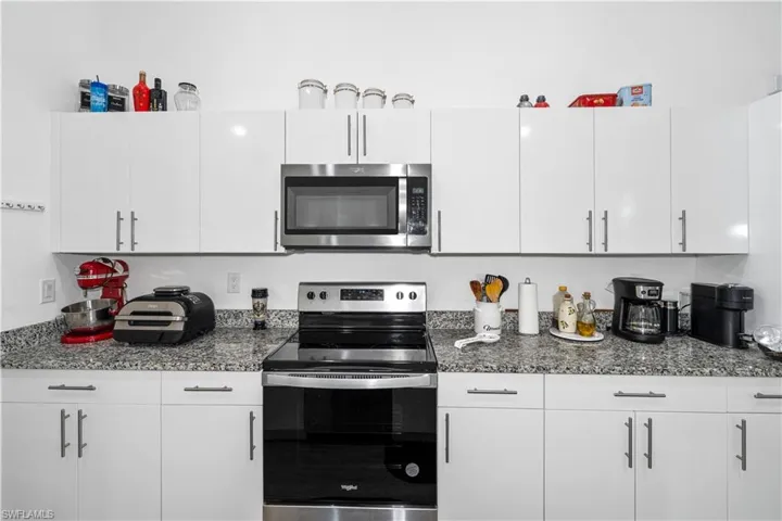 Kitchen with appliances with stainless steel finishes, dark stone countertops, and white cabinets