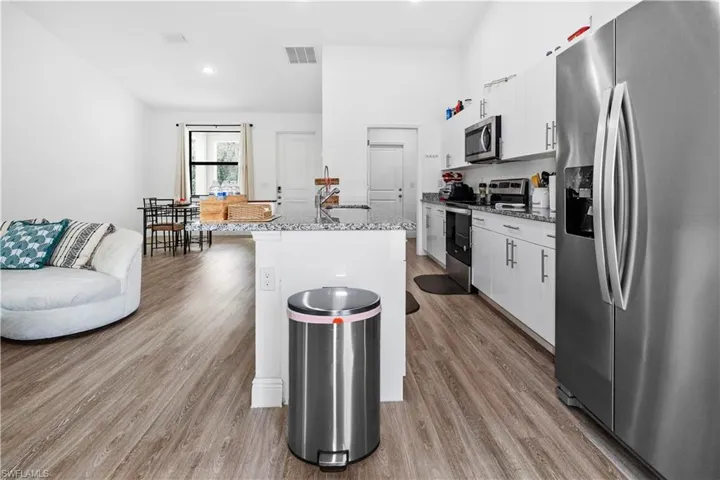 Kitchen featuring stainless steel appliances, white cabinets, light stone counters, light wood finished floors, and a kitchen island with sink