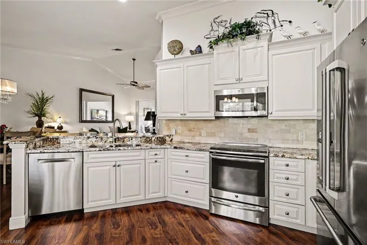 Kitchen with stainless steel appliances, white cabinetry, lofted ceiling, light stone countertops, and a peninsula