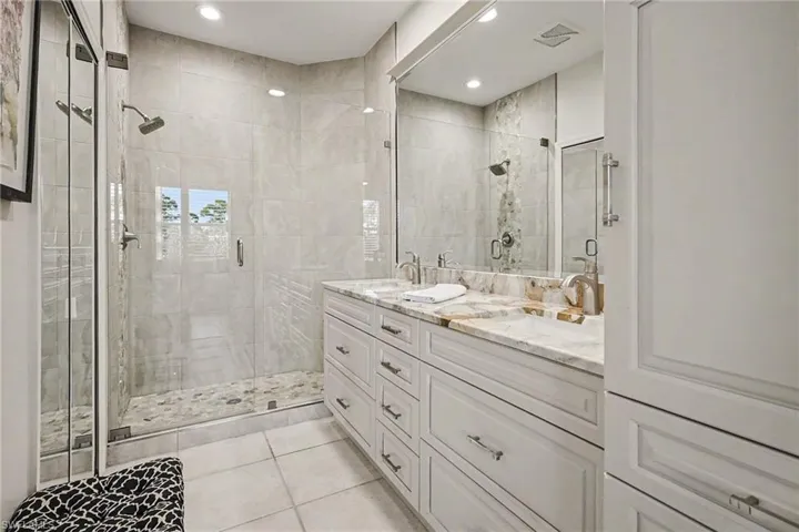 Bathroom featuring double vanity, a stall shower, light tile patterned flooring, and recessed lighting