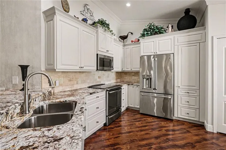 Kitchen with stainless steel appliances, white cabinetry, light stone counters, dark wood finished floors, and backsplash