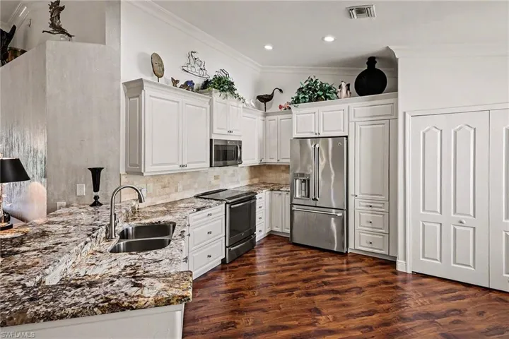 Kitchen with appliances with stainless steel finishes, dark stone counters, white cabinets, crown molding, and dark wood-type flooring