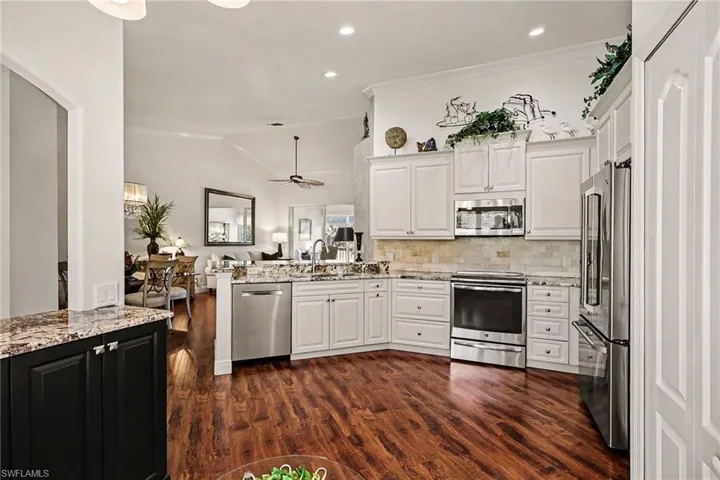Kitchen featuring appliances with stainless steel finishes, vaulted ceiling, light stone counters, white cabinetry, and crown molding