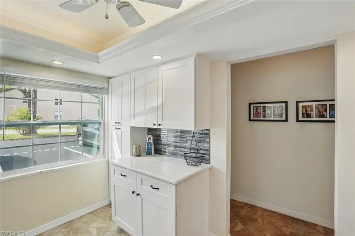 Kitchen with ornamental molding, backsplash, white cabinetry, light countertops, and baseboards