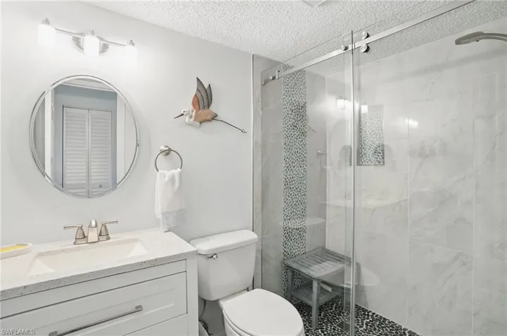 Bathroom featuring a textured ceiling, toilet, vanity, and a stall shower