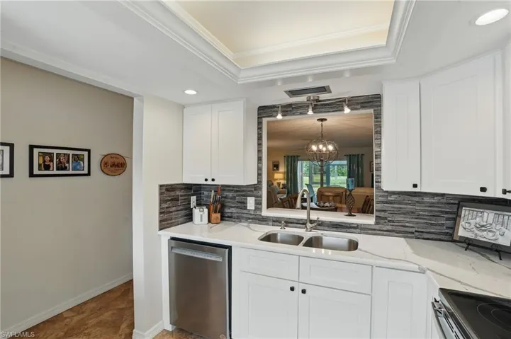 Kitchen with stainless steel appliances, a sink, backsplash, a tray ceiling, and crown molding