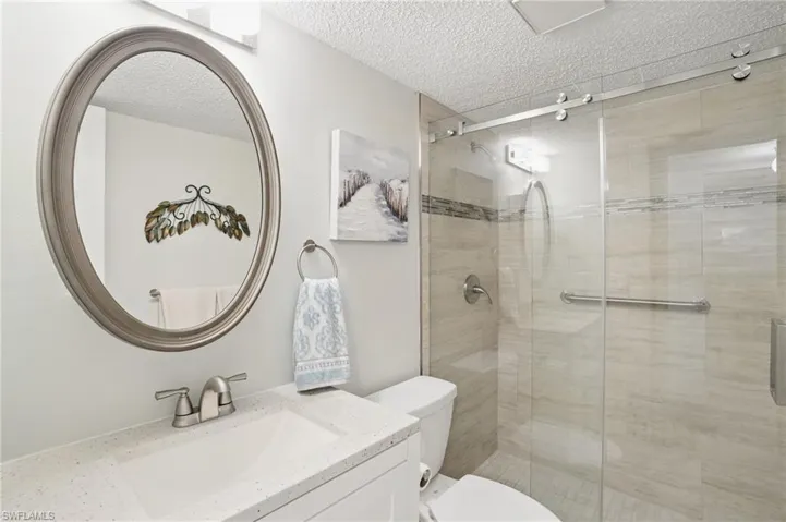 Bathroom featuring a textured ceiling, toilet, a shower stall, and vanity