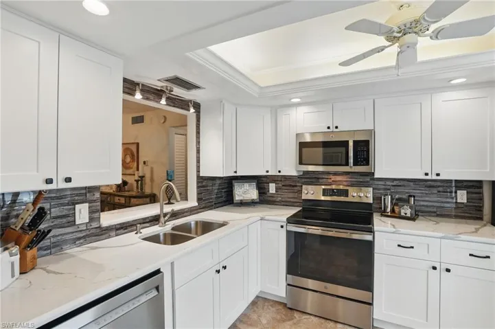 Kitchen featuring appliances with stainless steel finishes, a sink, a tray ceiling, tasteful backsplash, and white cabinets