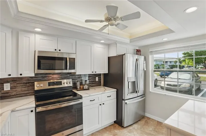 Kitchen with appliances with stainless steel finishes, a tray ceiling, ornamental molding, white cabinetry, and decorative backsplash
