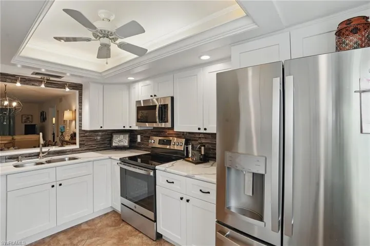 Kitchen with appliances with stainless steel finishes, a raised ceiling, a sink, tasteful backsplash, and white cabinets