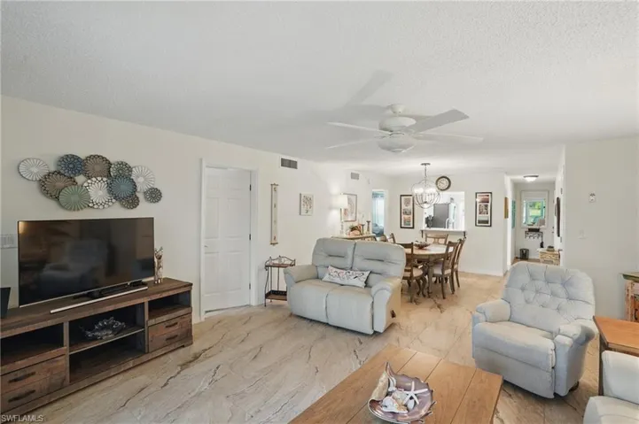 Living room with a ceiling fan, light marble finish floors, and a textured ceiling
