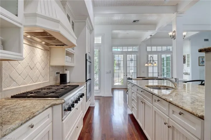 Kitchen with dark wood-type flooring, sink, decorative backsplash, french doors, and premium range hood