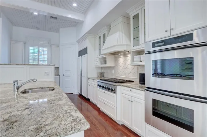 Kitchen with white cabinets, beam ceiling, appliances with stainless steel finishes, dark hardwood / wood-style flooring, and light stone countertops