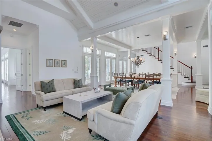 Living room featuring beamed ceiling, hardwood / wood-style floors, wooden ceiling, a notable chandelier, and ornate columns