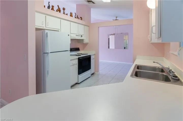 Kitchen featuring freestanding refrigerator, electric stove, vaulted ceiling, light tile patterned floors, and white cabinets
