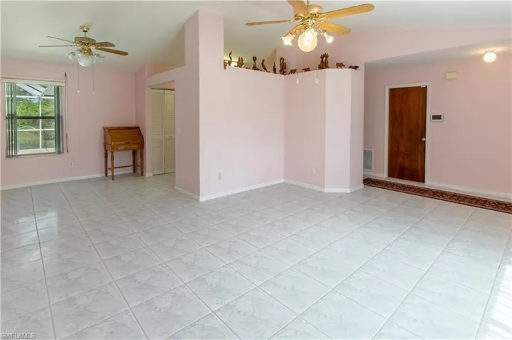 Empty room with a ceiling fan, vaulted ceiling, and light tile patterned floors