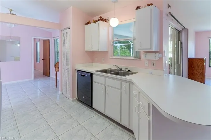 Kitchen with light countertops, black dishwasher, hanging light fixtures, white cabinets, and light tile patterned floors