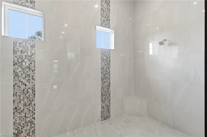 Spacious shower enclosure featuring large-format tile walls, decorative vertical mosaic tile accents, and integrated windows