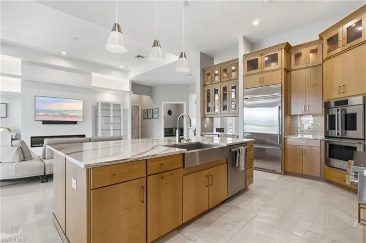 Spacious kitchen featuring a large central island with a farmhouse-style sink, light wood cabinetry, stainless steel appliances, and a tile backsplash