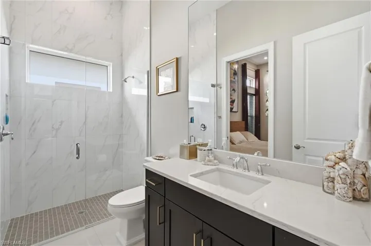 Spacious bathroom featuring a glass-enclosed shower with full-height white marble-look tile, a rectangular transom window, and a mosaic tile shower pan