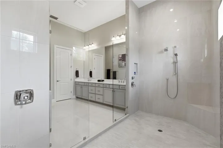 Spacious bathroom featuring a frameless glass shower enclosure with a built-in bench and a dual vanity with light gray cabinetry and a white countertop