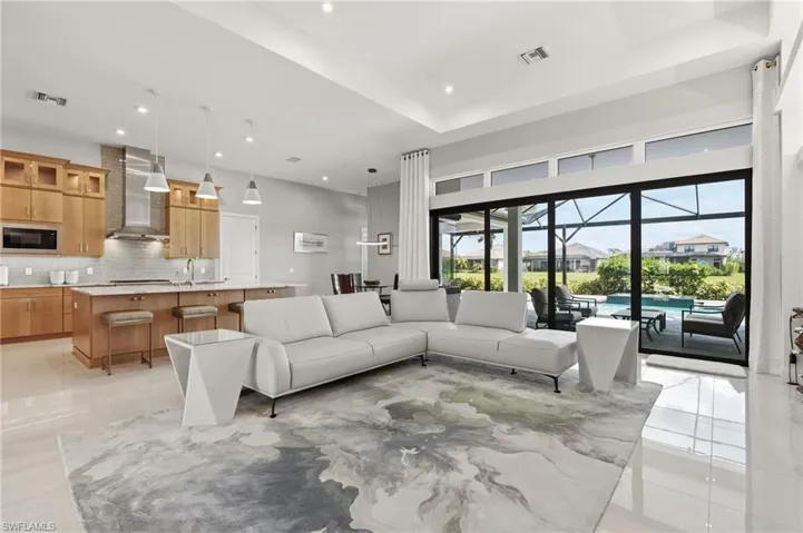 Open-concept living area featuring high ceilings, light wood cabinetry, a center island with seating, and a screened lanai with a swimming pool