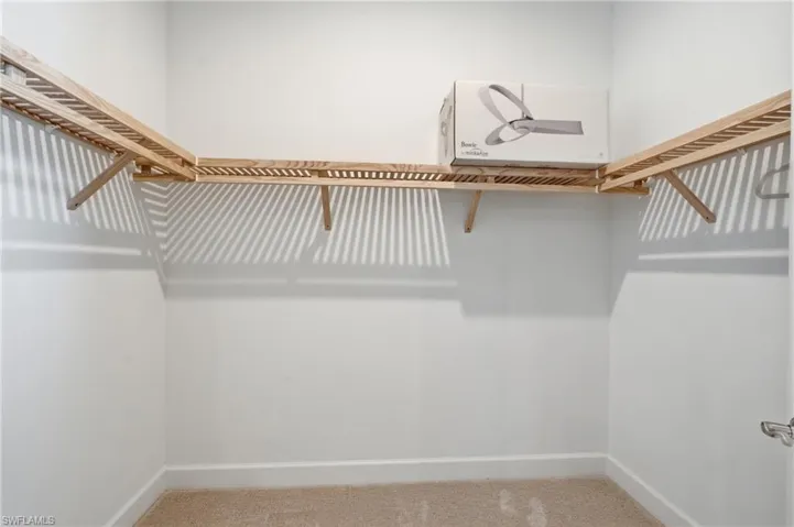 Walk-in closet featuring light wood shelving, white walls, and neutral carpet flooring