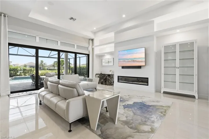 Spacious living area featuring large format polished tile flooring, a built-in linear electric fireplace, and expansive sliding glass doors opening to a screened lanai with a pool