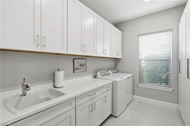 Utility room featuring extensive white shaker cabinetry, an integrated sink with a chrome faucet, a solid surface countertop, and light-toned flooring
