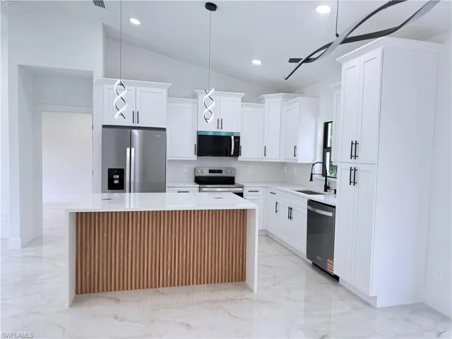 Kitchen with vaulted ceiling, stainless steel appliances, a kitchen island, light marble finish flooring, and light stone counters