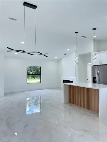 Kitchen with light marble finish flooring, hanging light fixtures, stainless steel fridge, light stone countertops, and a center island