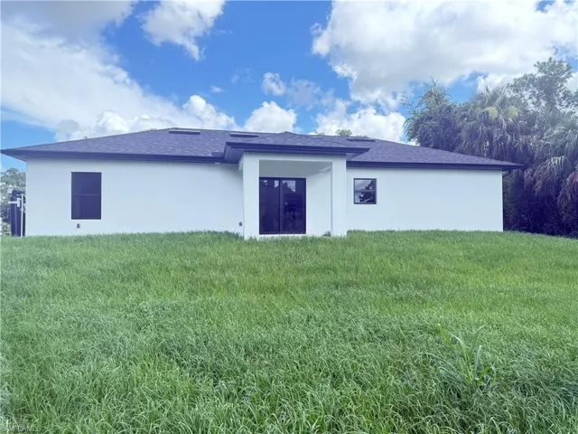 Rear view of property with stucco siding, a yard, and roof with shingles