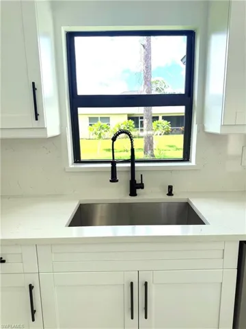 Kitchen with white cabinets, decorative backsplash, and light stone countertops