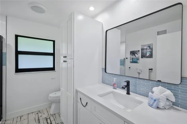 Full bathroom featuring vanity, backsplash, light wood-style floors, and recessed lighting