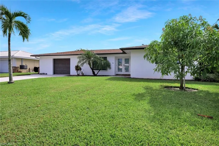 Single story home featuring driveway, a garage, stucco siding, and a front lawn
