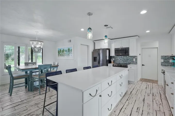 Kitchen with a breakfast bar, hanging light fixtures, decorative backsplash, white cabinets, and appliances with stainless steel finishes