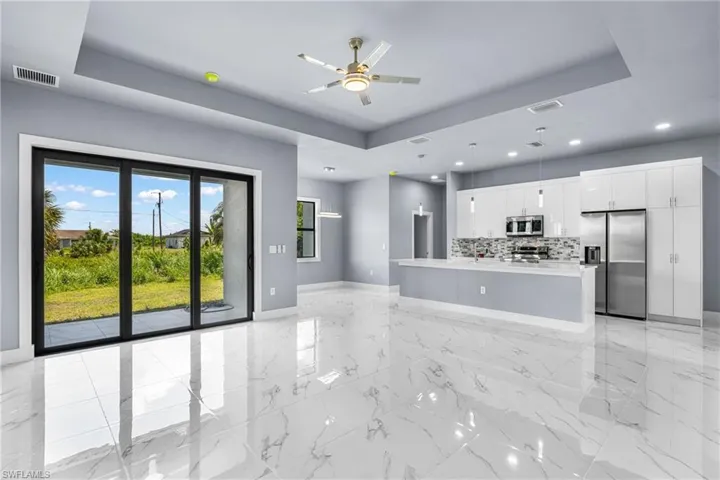 Open concept living area featuring large format tile flooring, a tray ceiling with a ceiling fan, and sliding glass doors