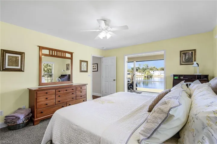 The large master suite has French doors to the lanai, lake view, carpet, a large walk-in closet, bright white quartz countertop with makeup setting area, classy fixtures with dual mirrors, shower tub combination, and linen closet for extra storage