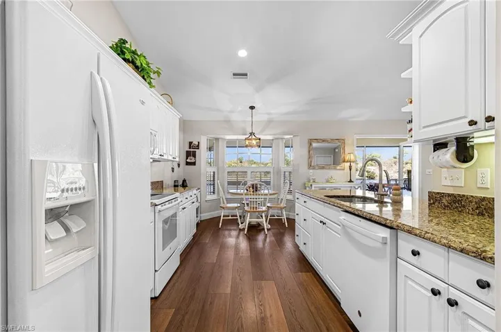 The lovely kitchen has granite countertops, white raised panel cabinets, white appliances, pantry closet off kitchen, and a breakfast nook with plantation shutters