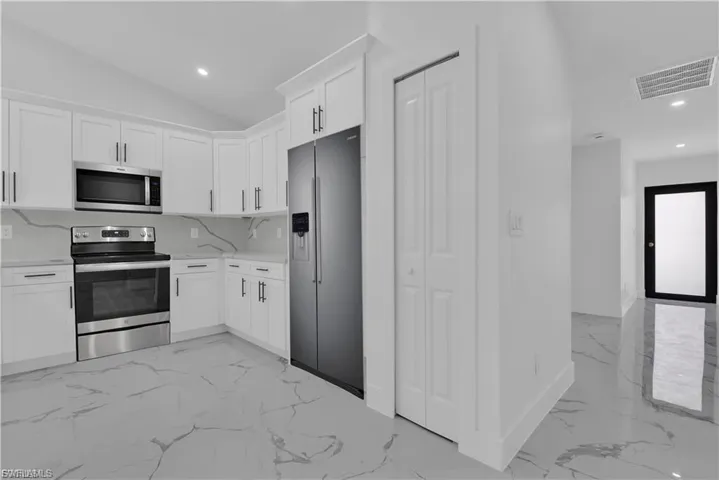 Kitchen with stainless steel appliances, white cabinets, recessed lighting, light marble finish flooring, and light stone countertops