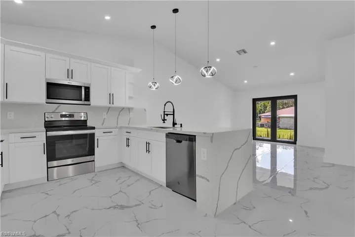 Kitchen featuring stainless steel appliances, light stone countertops, a peninsula, white cabinets, and vaulted ceiling