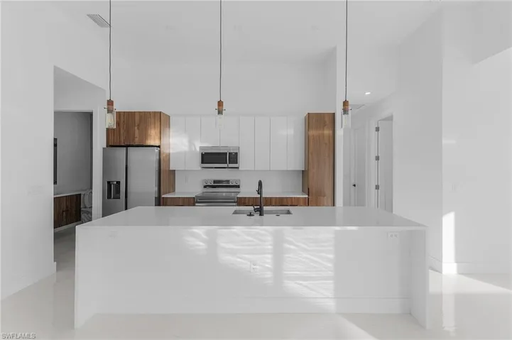 Kitchen with an island with sink, white cabinetry, appliances with stainless steel finishes, modern cabinets, and light stone countertops