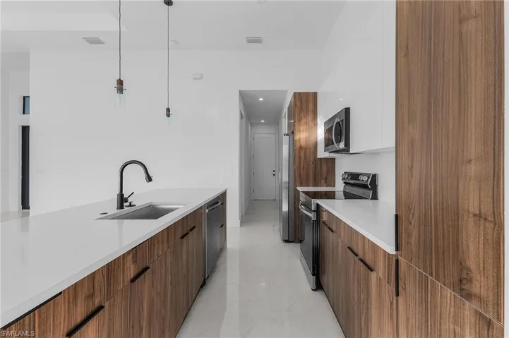 Kitchen featuring modern cabinets, brown cabinetry, stainless steel appliances, hanging light fixtures, and light stone countertops